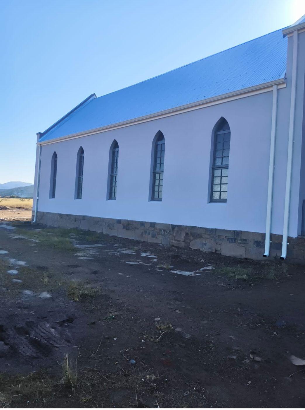 The restored church from outside — white walls, new roof and arched windows above the stone plinth