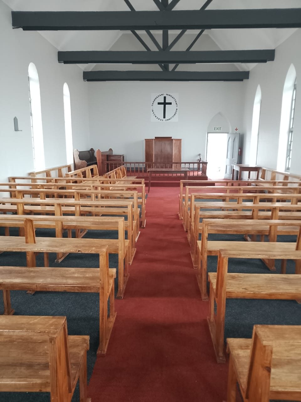 The renovated church interior with white walls, dark steel trusses, timber pews and a red carpet aisle