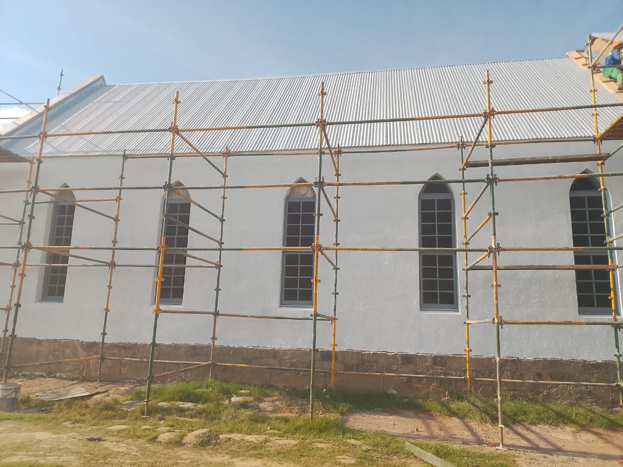 The church wrapped in scaffolding during renovation, with fresh white walls, a new corrugated roof and new arched windows